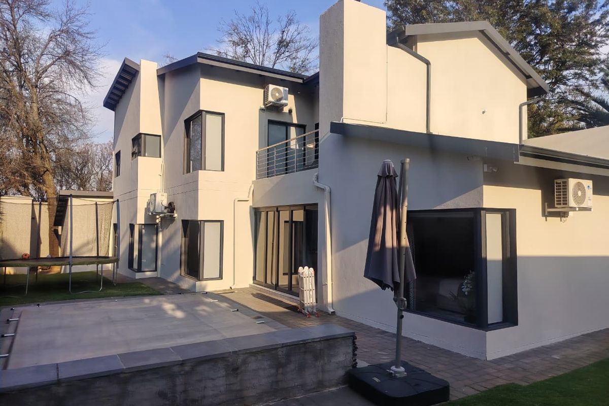 Rear view of a modern two-story house featuring a paved patio, balcony, and exterior air conditioning units.