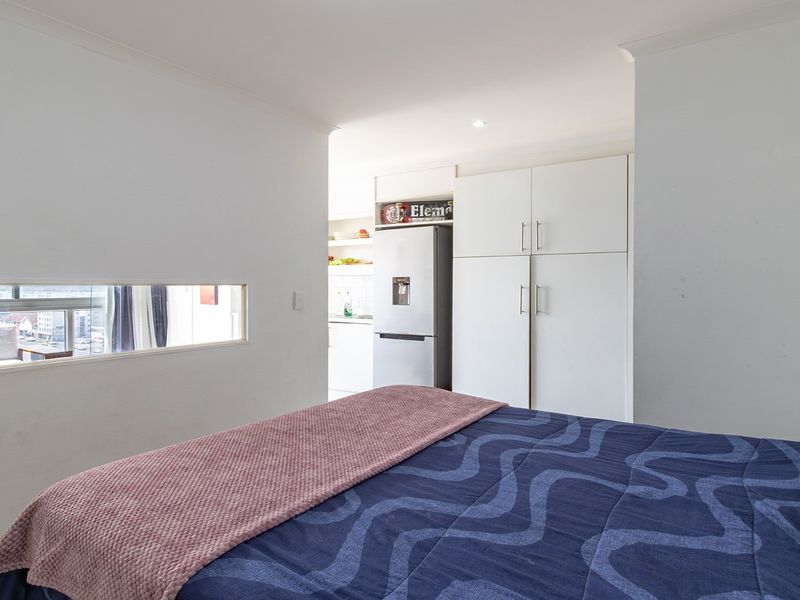 A bedroom featuring built-in cupboards and a unique horizontal window, with an open transition to an adjacent kitchen area.