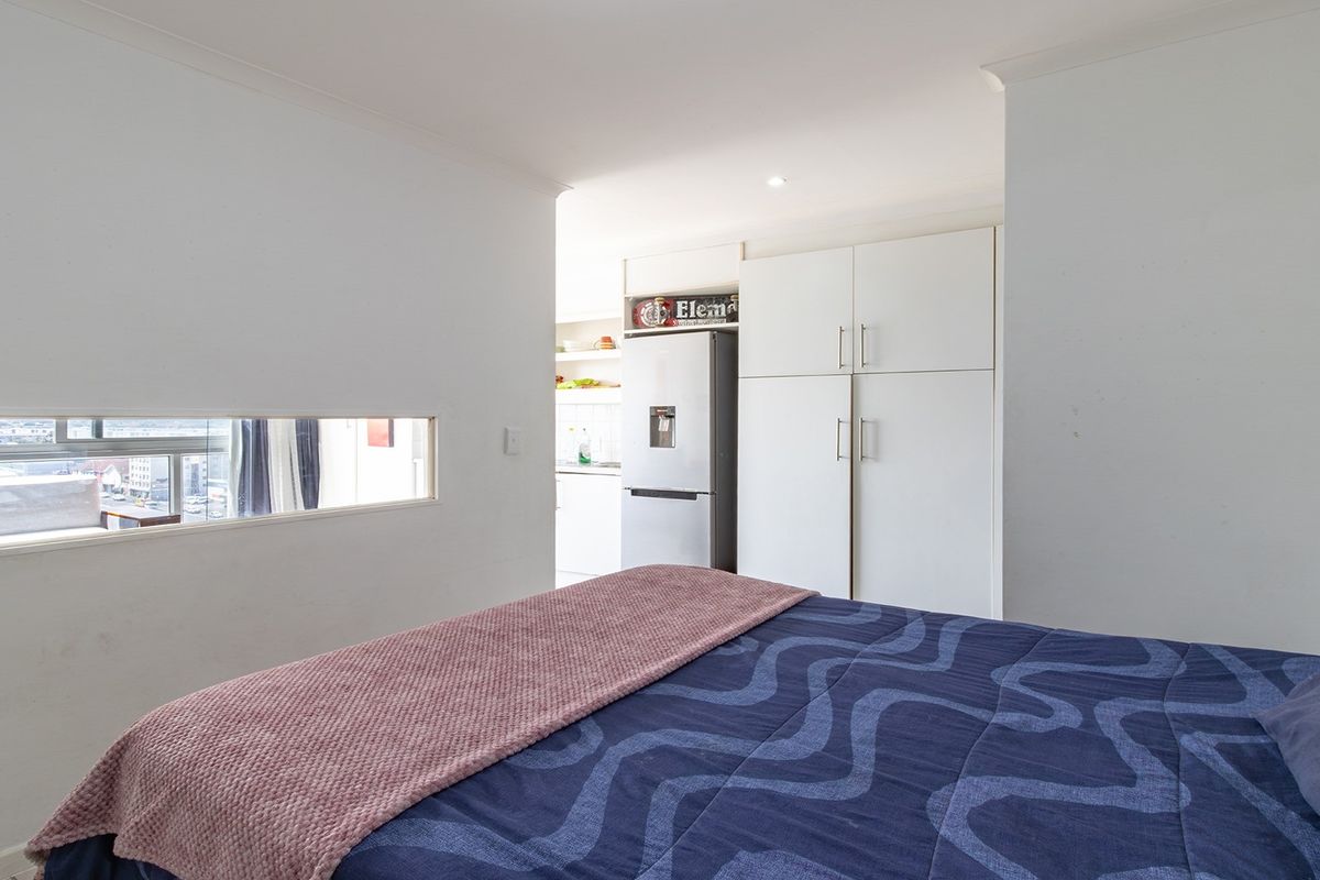 A bedroom featuring built-in cupboards and a unique horizontal window, with an open transition to an adjacent kitchen area.