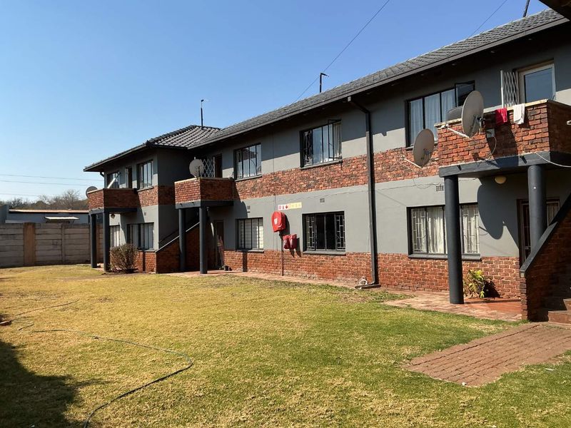Rear view of a multi-story apartment complex featuring brick and plaster facade, private balconies, and a shared garden area.