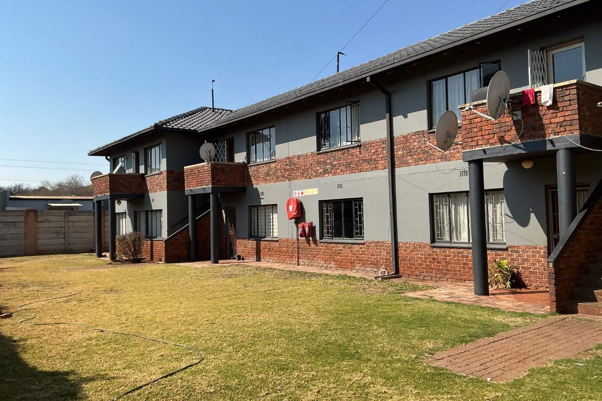 Rear view of a multi-story apartment complex featuring brick and plaster facade, private balconies, and a shared garden area.