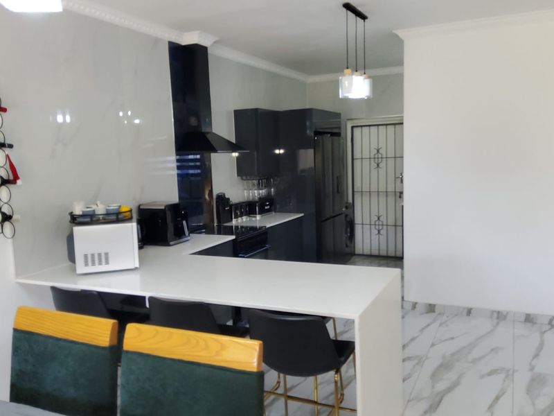 Modern kitchen featuring sleek dark cabinetry, white quartz countertops, a breakfast bar, and marble-look floor tiles with a clean, contemporary aesthetic.