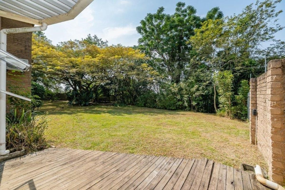 A rear view of the townhouse featuring a timber deck patio overlooking a private garden with mature trees and a brick boundary wall.