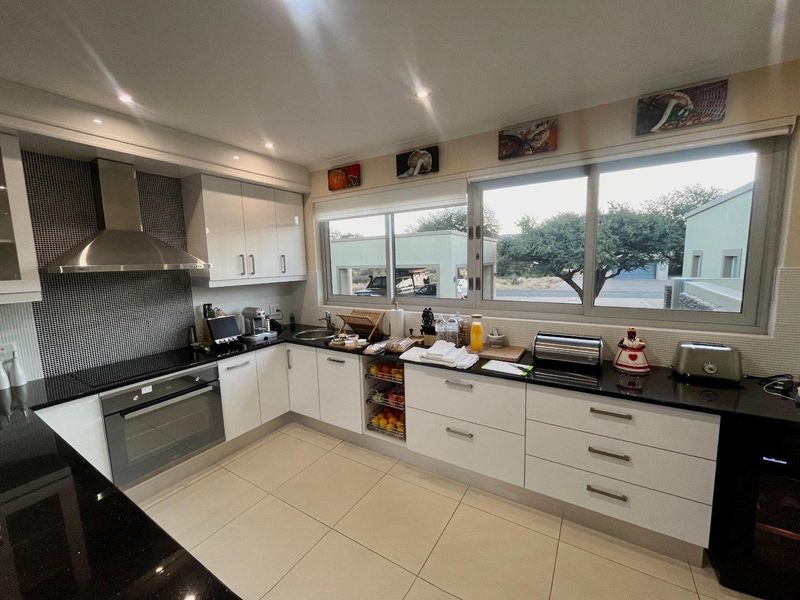 Modern kitchen featuring white cabinetry, black granite countertops, mosaic tile backsplash, built-in oven, and large windows providing natural light.