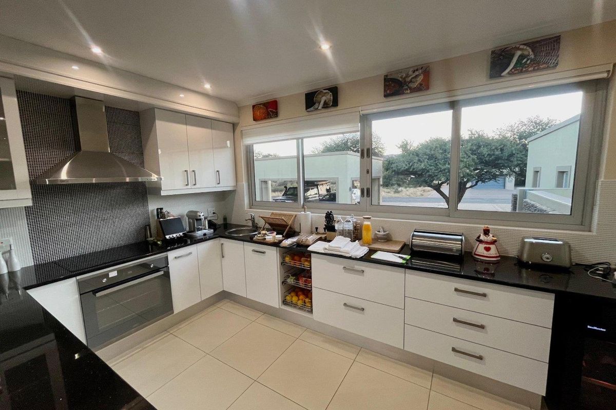 Modern kitchen featuring white cabinetry, black granite countertops, mosaic tile backsplash, built-in oven, and large windows providing natural light.