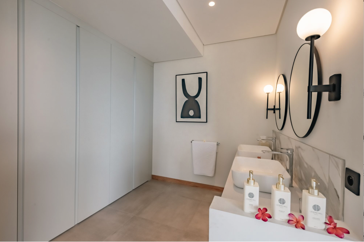 Modern bathroom featuring a double vanity with vessel sinks, marble-look backsplash, wall-mounted lighting, and extensive floor-to-ceiling built-in cabinetry.