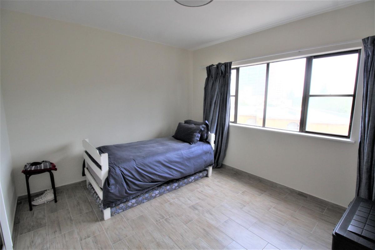 A simple bedroom featuring neutral wall paint, tiled flooring, and a large window that provides natural light.