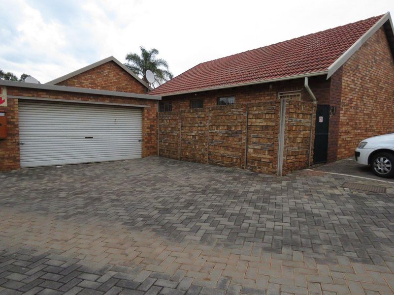 Front exterior view of the townhouse featuring a brick facade, tiled roof, paved driveway, and a secure roller garage door.
