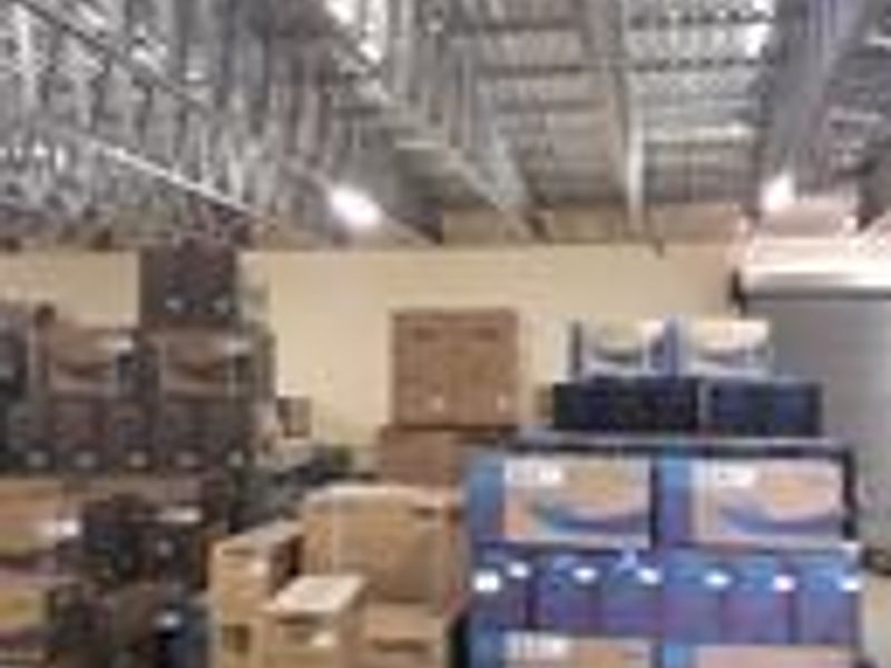 Industrial utility space featuring exposed steel roof trusses, concrete flooring, and a roller shutter door, currently utilized for storage.