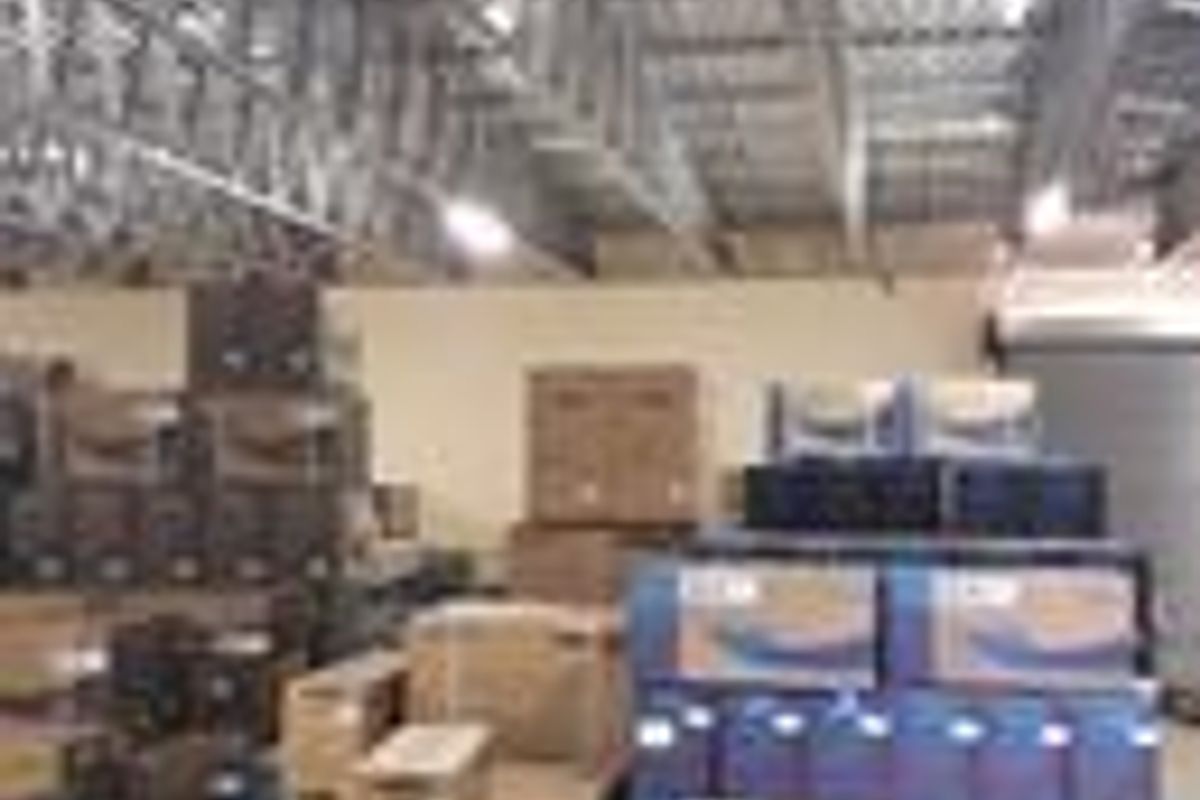 Industrial utility space featuring exposed steel roof trusses, concrete flooring, and a roller shutter door, currently utilized for storage.