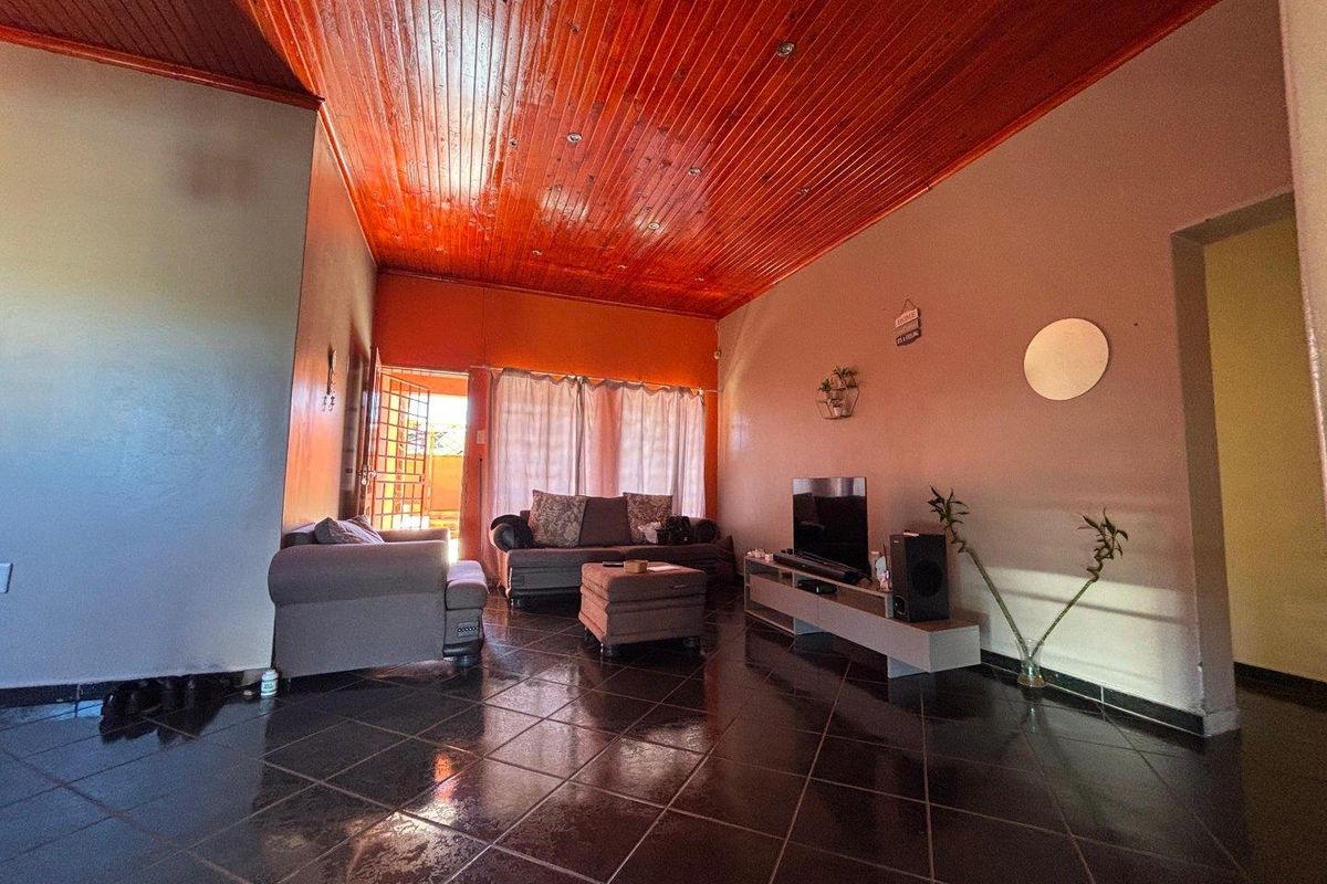 A living room featuring dark tiled flooring and a distinctive timber-paneled ceiling, providing a warm and rustic aesthetic to the main living space.