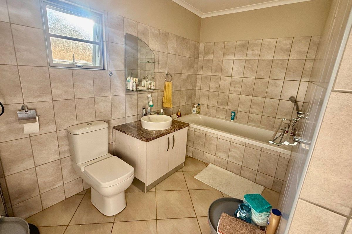 A functional bathroom featuring a built-in bathtub, a vanity with a vessel sink, a toilet, and neutral wall and floor tiling.