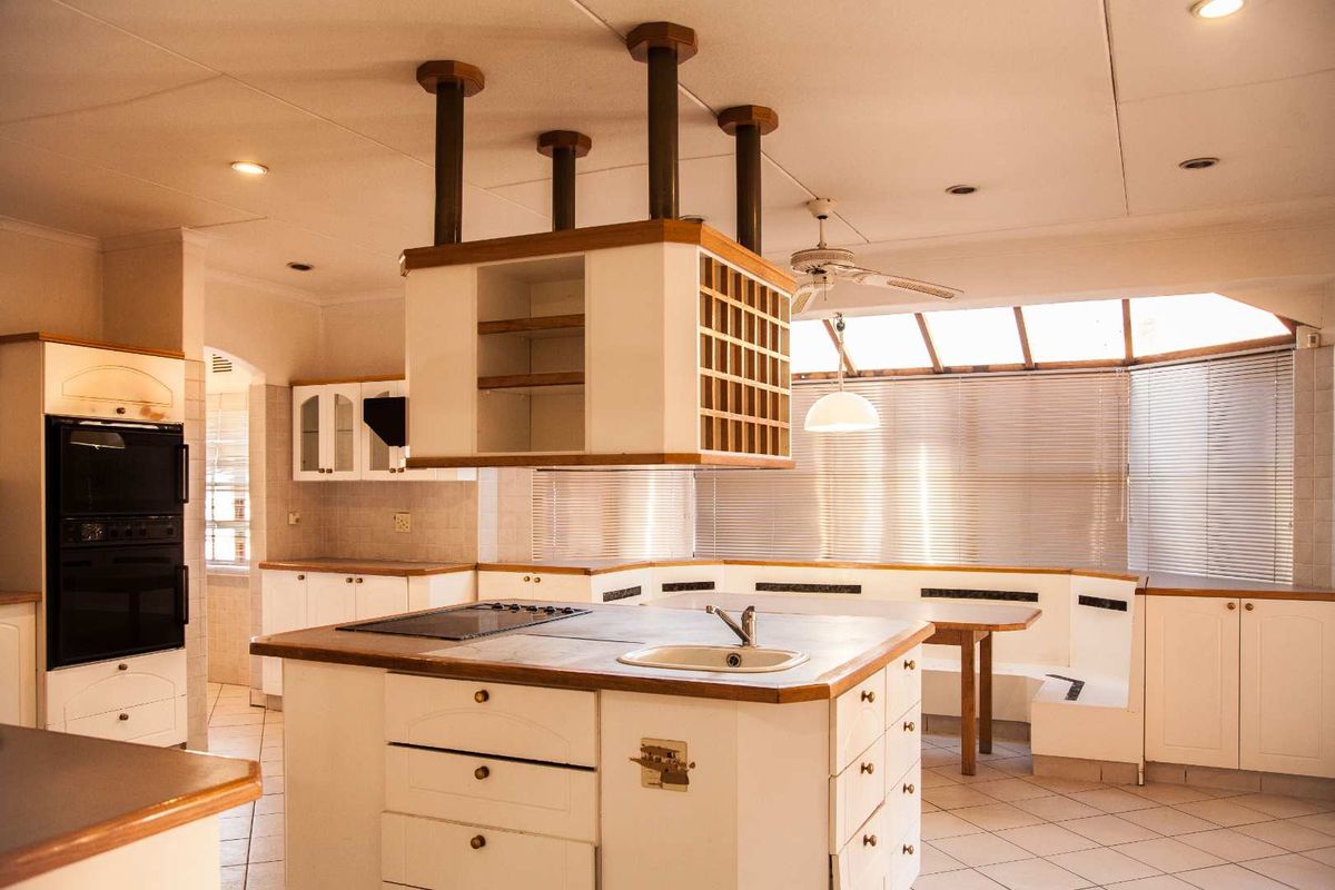 Spacious kitchen featuring a central island with integrated sink and hob, overhead storage unit, and built-in breakfast nook with tiled flooring.
