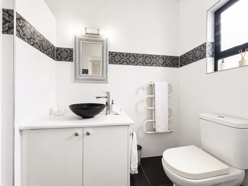 Modern bathroom featuring a sleek vessel sink, vanity cabinet, heated towel rail, and stylish decorative wall tiling.