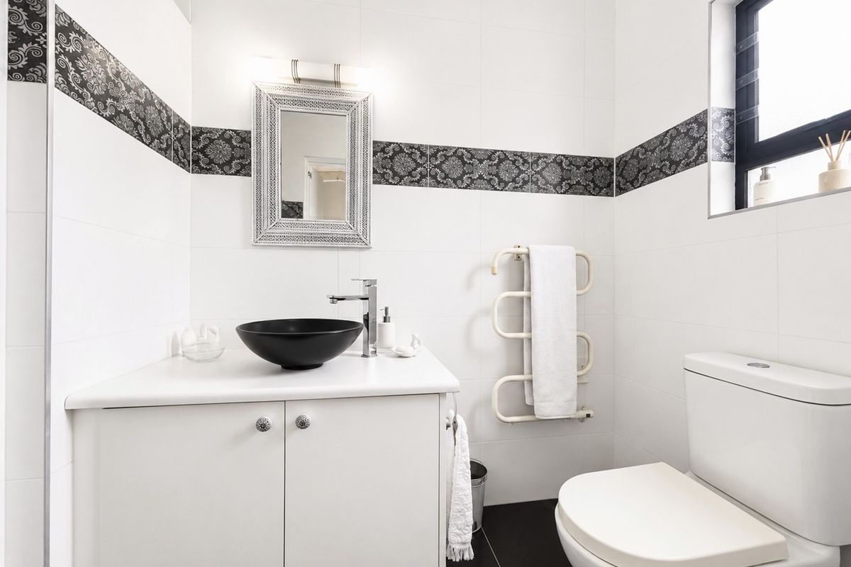 Modern bathroom featuring a sleek vessel sink, vanity cabinet, heated towel rail, and stylish decorative wall tiling.