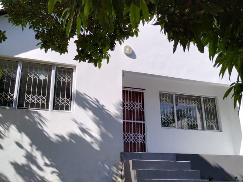 Front elevation of the cottage featuring white exterior walls, security gates, and window security bars, accessed by a set of concrete steps.
