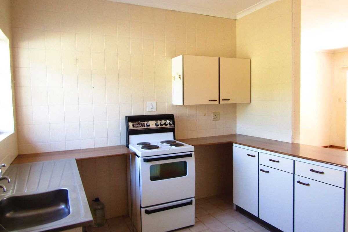 A dated kitchen featuring original cabinetry, laminate countertops, a stainless steel sink, and a freestanding stove, offering potential for modernization.