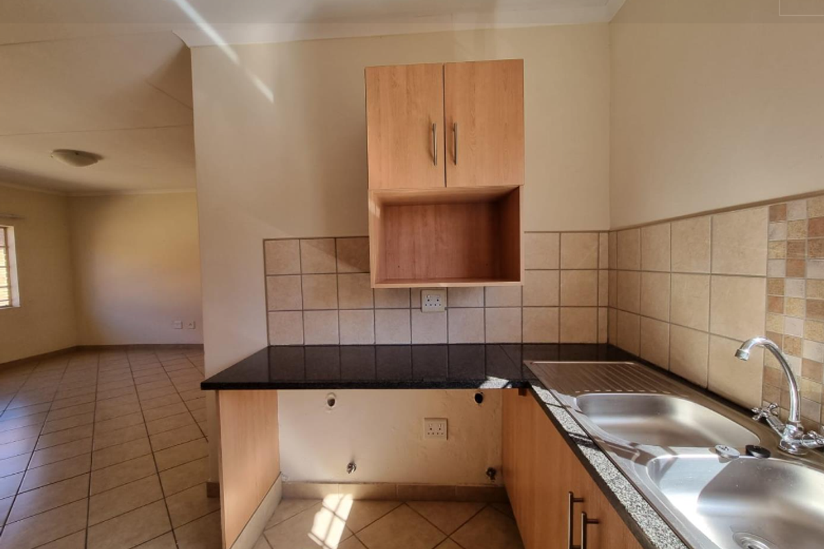 A functional kitchen area featuring dark granite countertops, a double stainless steel sink, and light wood cabinetry with tiled splashbacks.