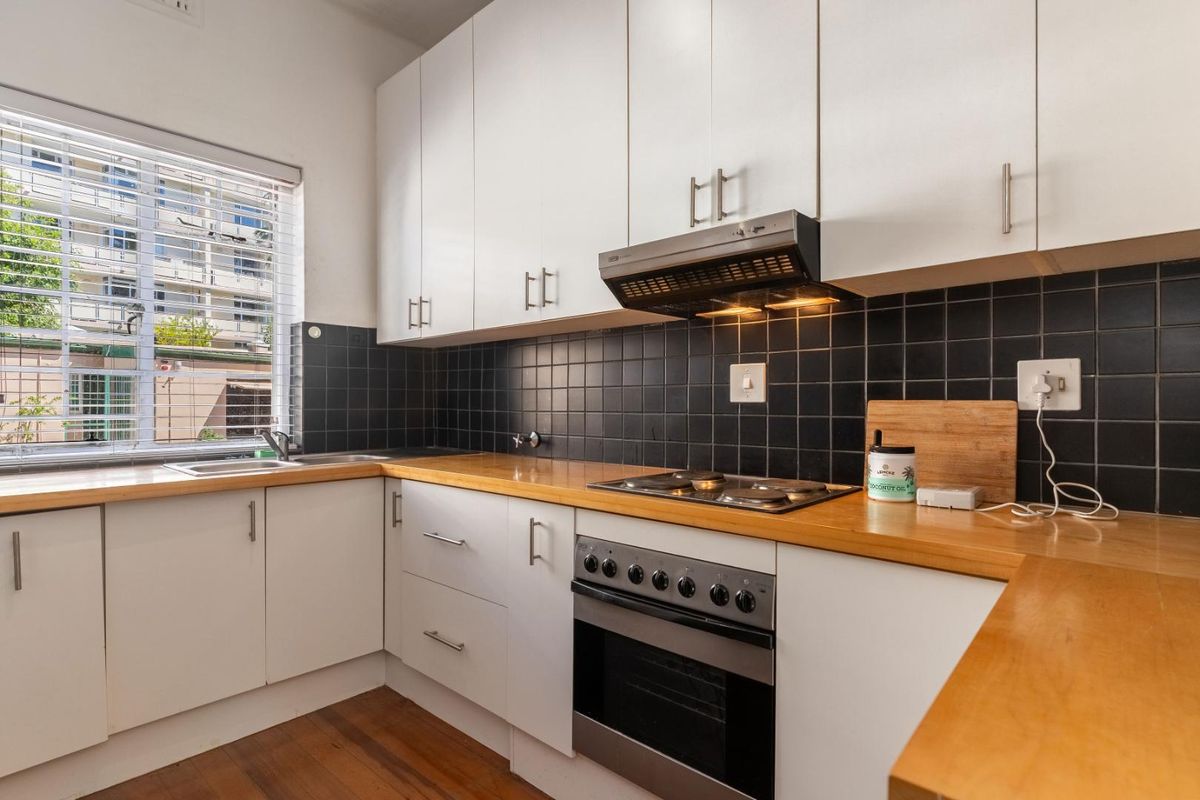 A functional kitchen featuring white cabinetry, wooden countertops, a built-in oven with hob, extractor fan, and a tiled backsplash.