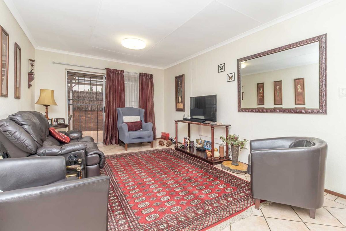 A comfortable living room featuring tiled flooring and a sliding glass door with security gate, providing access to the outdoor area.