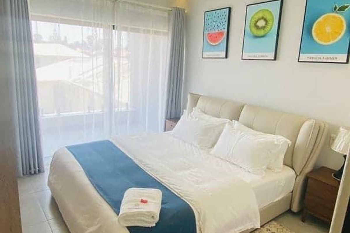 A well-maintained hotel bedroom featuring tiled flooring, recessed ceiling lighting, and a large sliding glass door providing access to a private balcony.