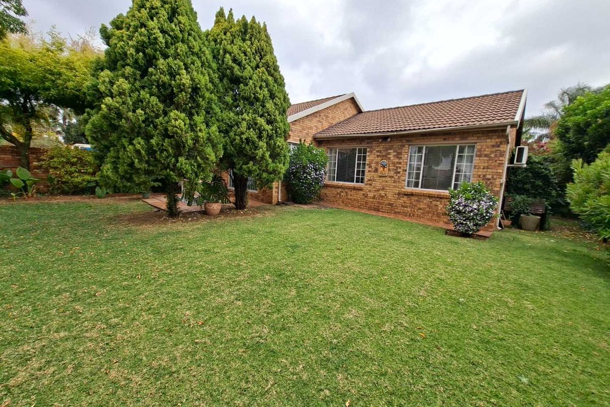 A view of the rear exterior of the townhouse, featuring a brick facade, tiled roof, and a well-maintained garden area.
