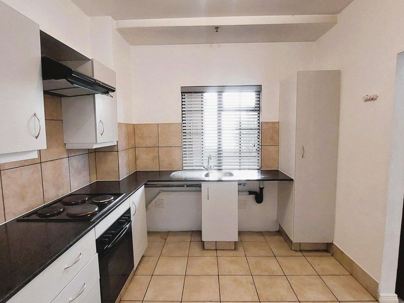 A functional kitchen featuring built-in cabinetry, an electric hob, oven, extractor fan, and tiled finishes throughout.