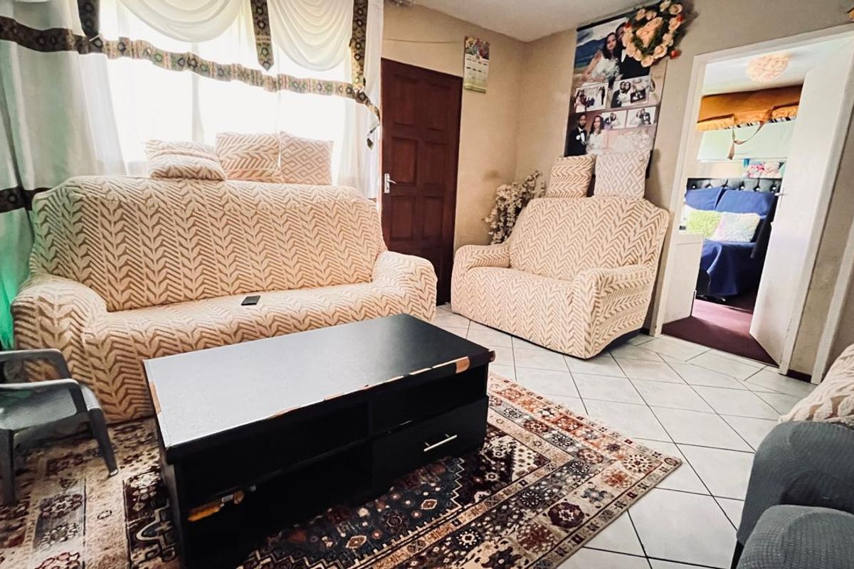 A living room featuring tiled flooring and a doorway leading to an adjacent bedroom.