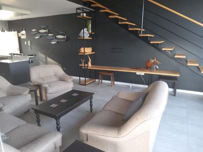 Modern open-plan living area featuring a striking floating staircase, built-in shelving, and a sleek kitchen island with contemporary tiled flooring.