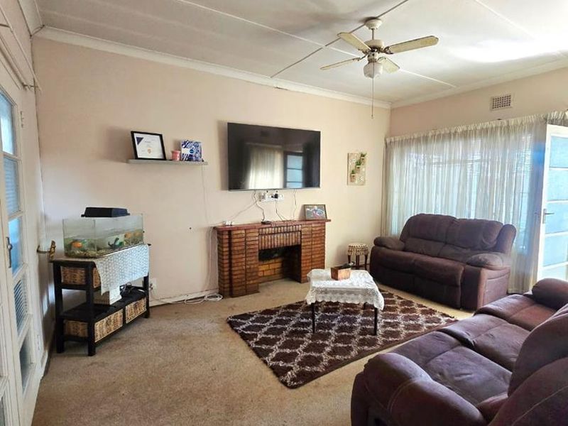 A living room featuring a brick fireplace, ceiling fan, and tiled ceiling, with worn carpeting throughout the space.