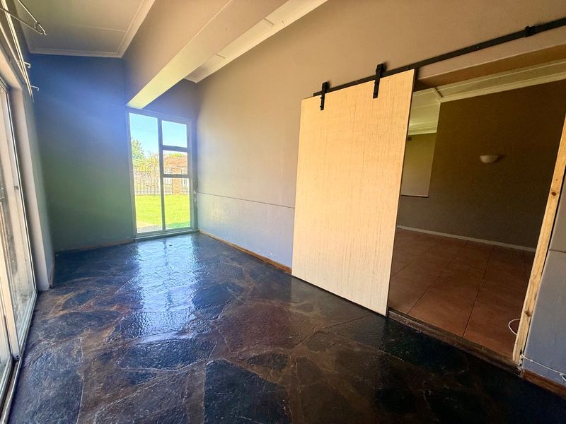An empty living area featuring unique stone flooring, a modern sliding barn door, and large aluminium sliding doors providing access to the garden.