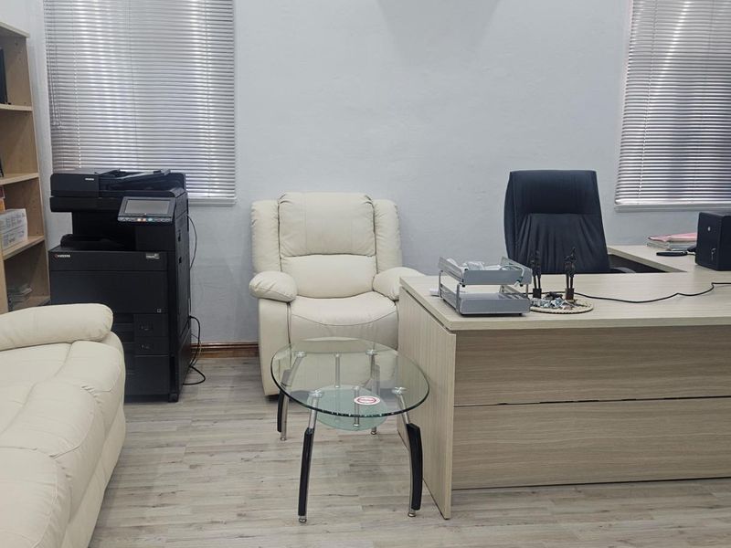 A functional office space featuring light wood-look flooring, horizontal window blinds, and built-in shelving units.