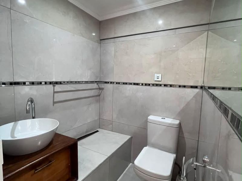 Modern office bathroom featuring large format grey wall tiles, a floating wooden vanity with a vessel sink, and a sleek toilet.