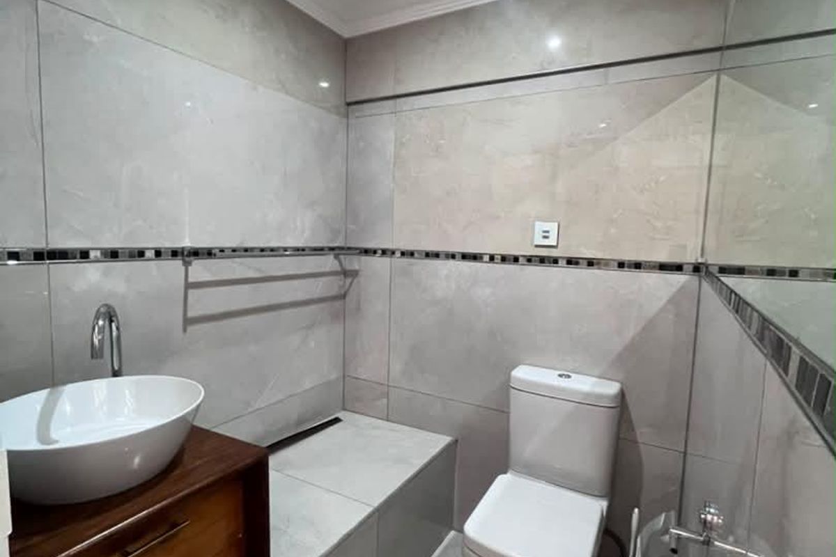Modern office bathroom featuring large format grey wall tiles, a floating wooden vanity with a vessel sink, and a sleek toilet.