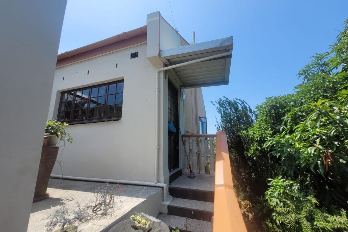 Rear exterior view of the property featuring a small covered landing, tiled steps with a railing, and a timber-framed window.