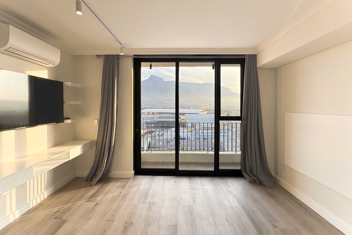 Bright and modern living area featuring light laminate flooring, track lighting, built-in shelving, and a sliding glass door leading to a balcony with mountain views.