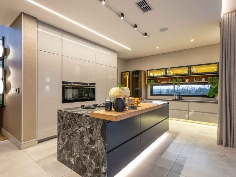 Modern luxury kitchen featuring a large stone-topped island, integrated high-end appliances, sleek cabinetry, and sophisticated ambient lighting throughout.