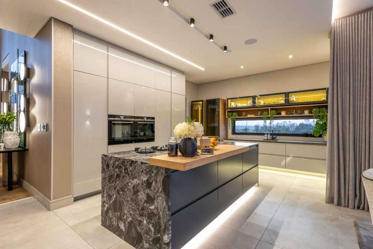 Modern luxury kitchen featuring a large stone-topped island, integrated high-end appliances, sleek cabinetry, and sophisticated ambient lighting throughout.