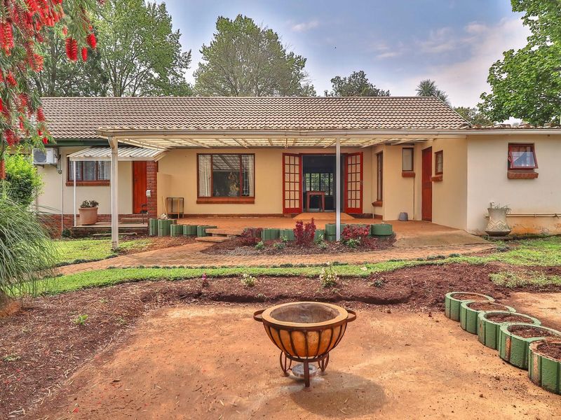 Rear view of a single-story house featuring a covered patio, brick paved area, and established garden space.