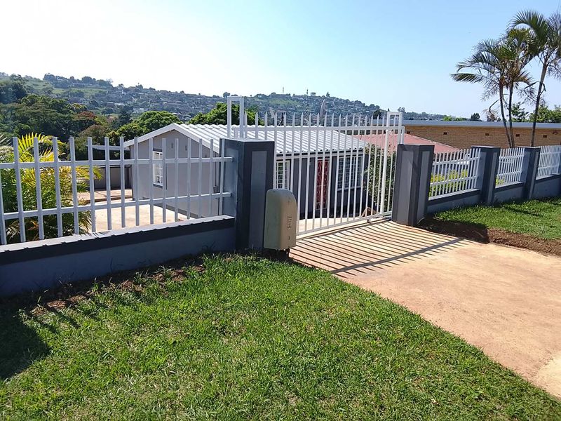 Front view of the property featuring a secure perimeter wall, motorized metal gate, and a paved driveway leading to the main house.