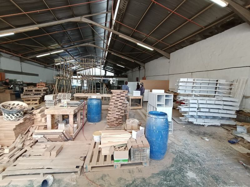 Spacious industrial workshop area featuring high ceilings with exposed steel trusses, fluorescent lighting, and durable concrete flooring, suitable for manufacturing or storage operations.