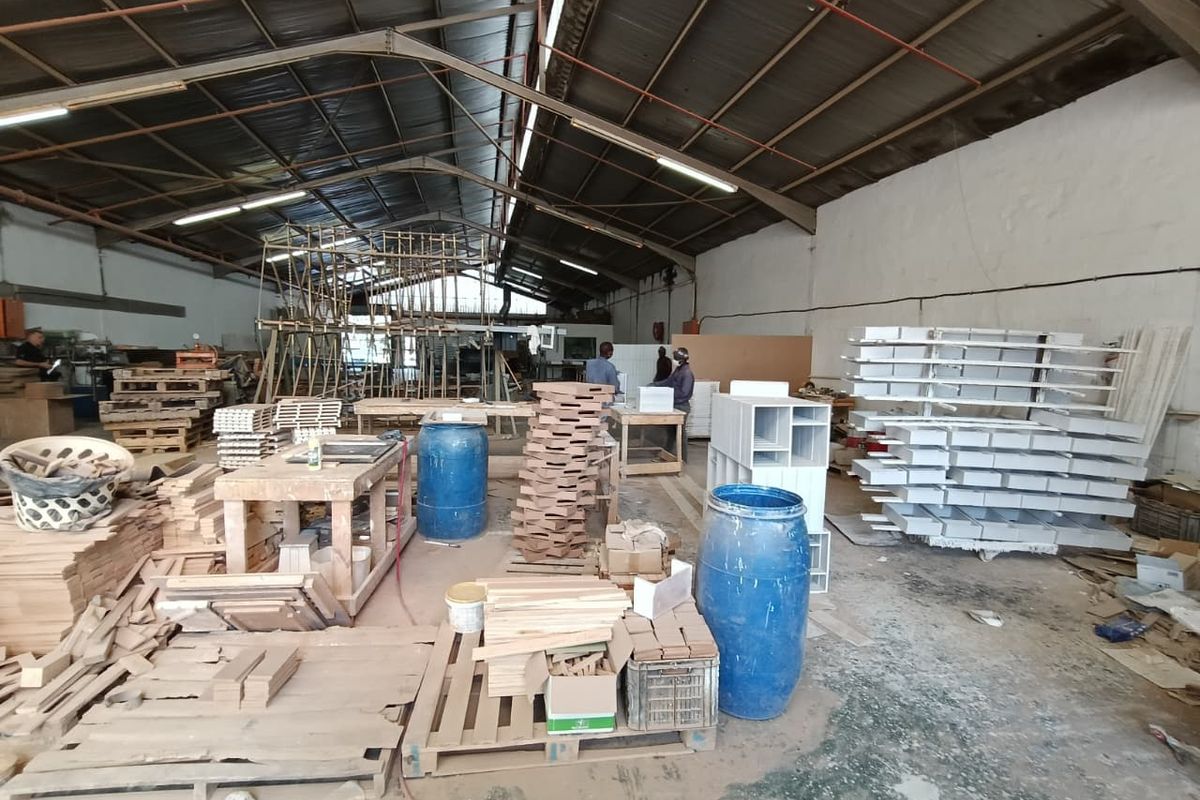 Spacious industrial workshop area featuring high ceilings with exposed steel trusses, fluorescent lighting, and durable concrete flooring, suitable for manufacturing or storage operations.