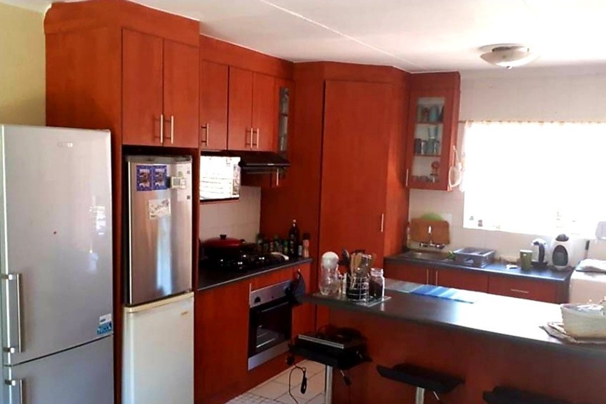 A functional kitchen featuring wooden cabinetry, a built-in oven and hob, a breakfast bar island, and a double sink with natural light.