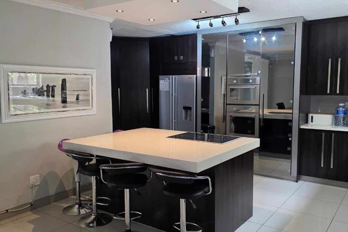 Modern kitchen featuring a central island with stone countertop, built-in hob, dark wood cabinetry, and integrated appliances with recessed ceiling lighting.