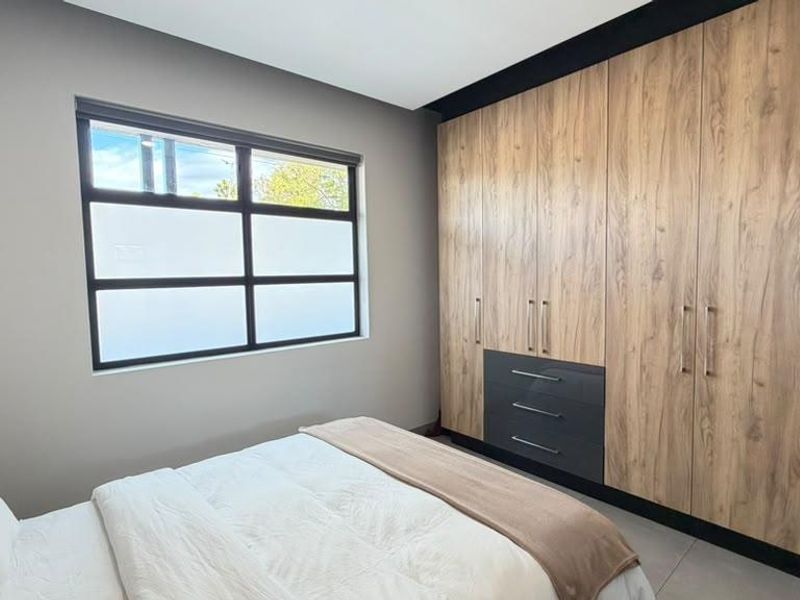A modern bedroom featuring high-quality built-in wooden cupboards, tiled flooring, and a large aluminium-framed window with frosted glass for privacy.
