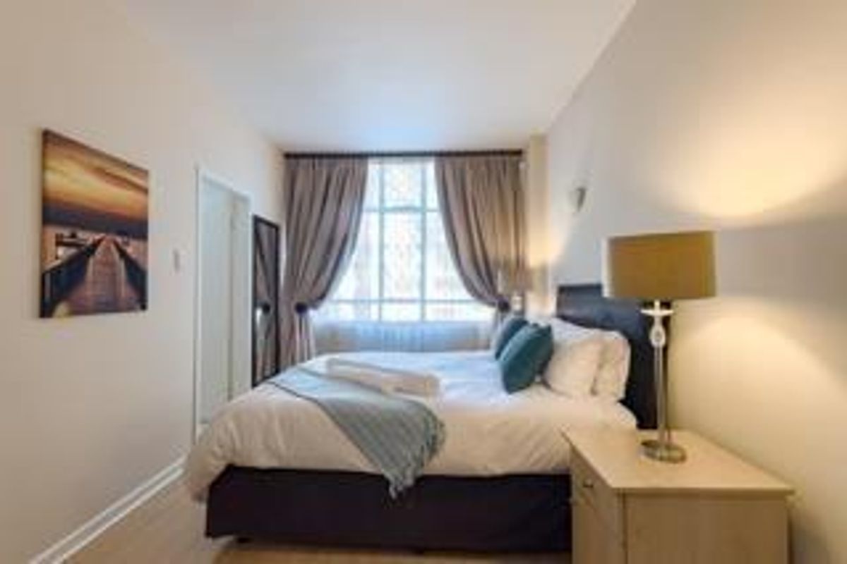 A well-lit bedroom featuring large windows with floor-to-ceiling curtains, neutral wall finishes, and light-toned flooring.