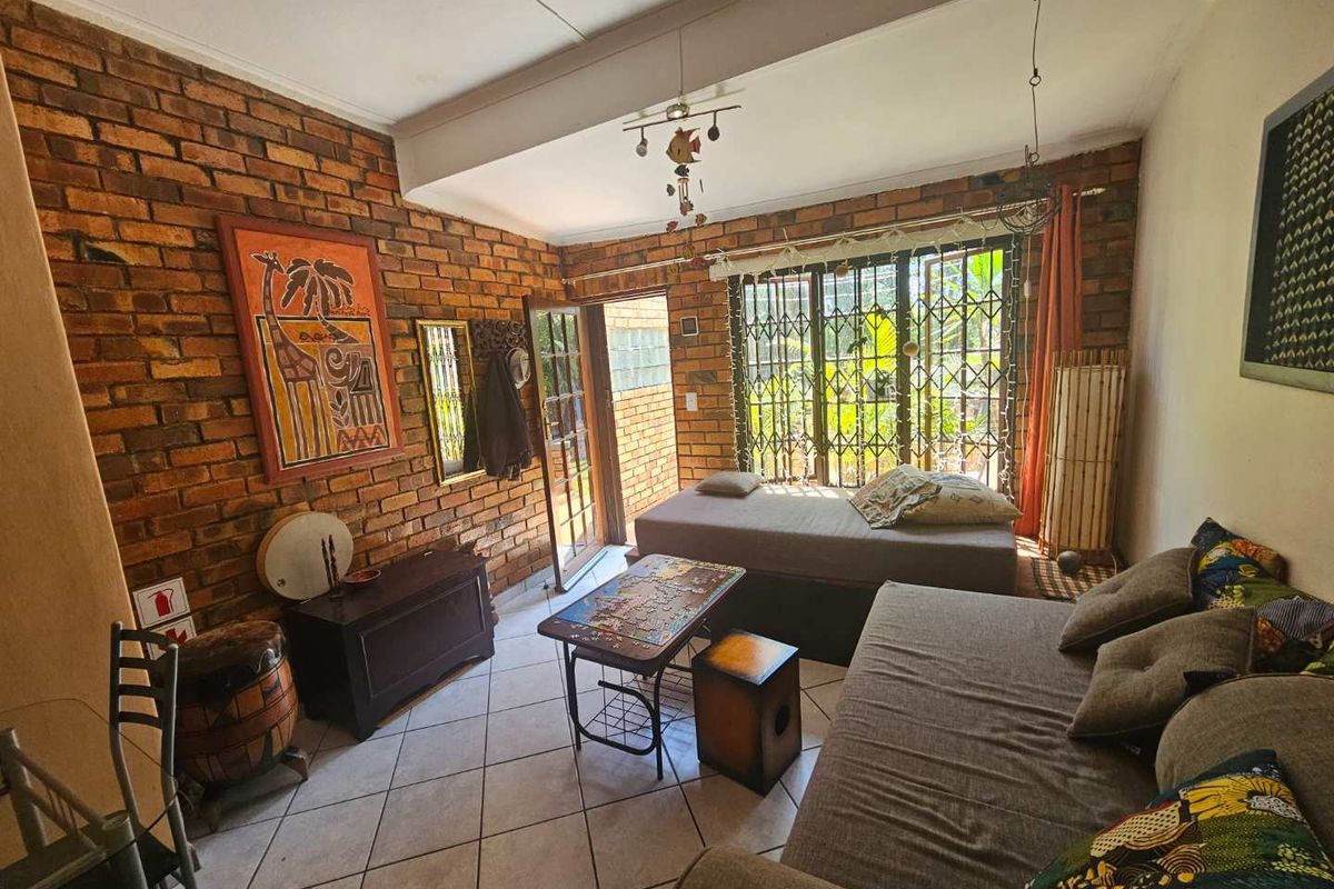 A living room featuring exposed brick walls, tiled flooring, and direct access to an outdoor area through a glass-paneled door.