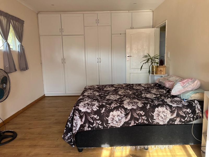 A bedroom featuring extensive white built-in cupboards for storage and durable laminate flooring, offering a functional and neutral living space.