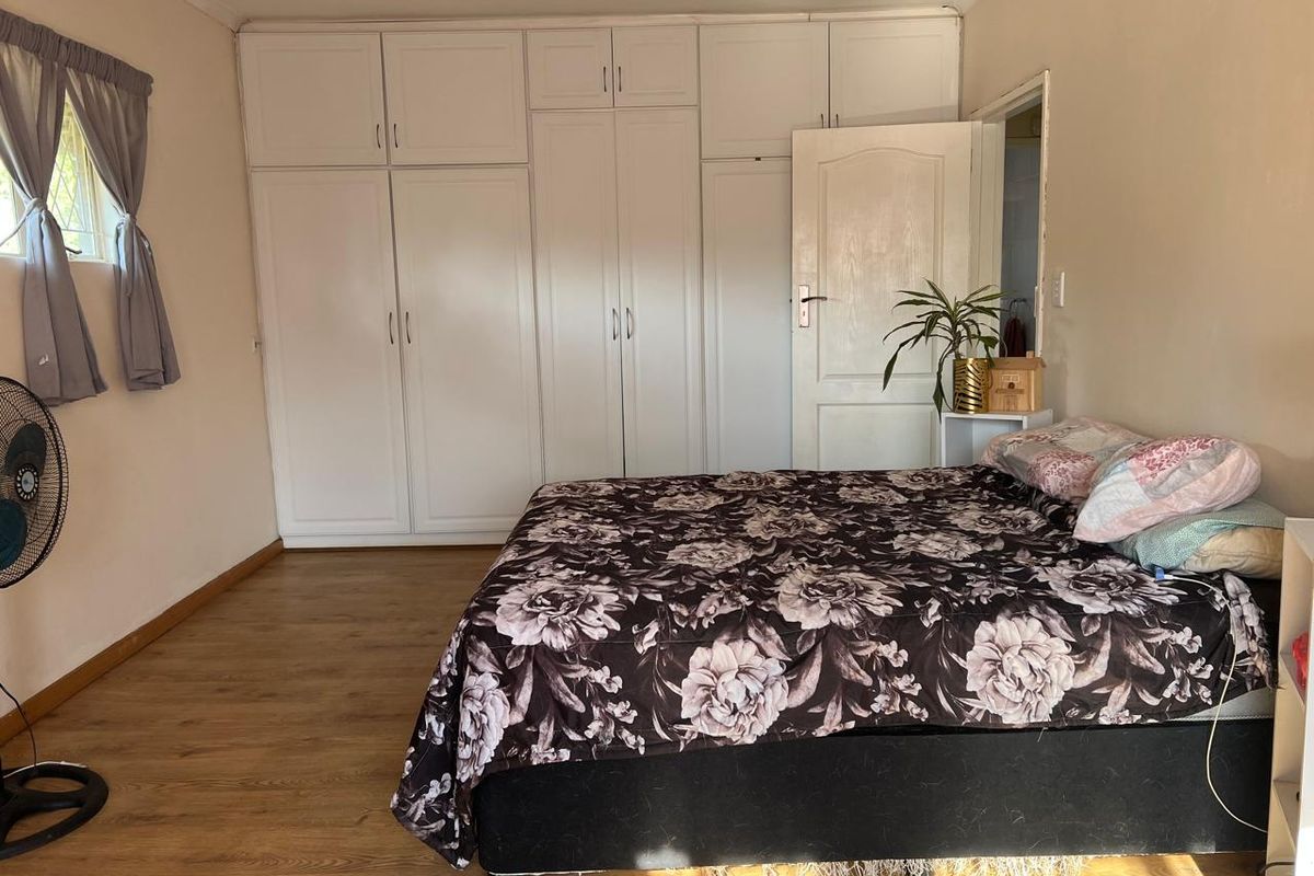 A bedroom featuring extensive white built-in cupboards for storage and durable laminate flooring, offering a functional and neutral living space.