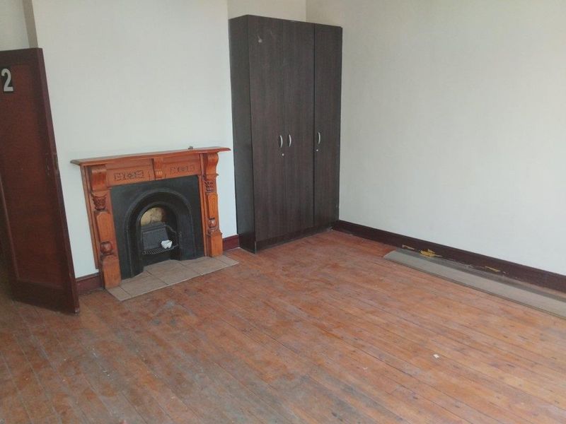 A bedroom featuring a traditional cast iron fireplace with a timber mantel and original timber flooring, requiring some cosmetic refurbishment.
